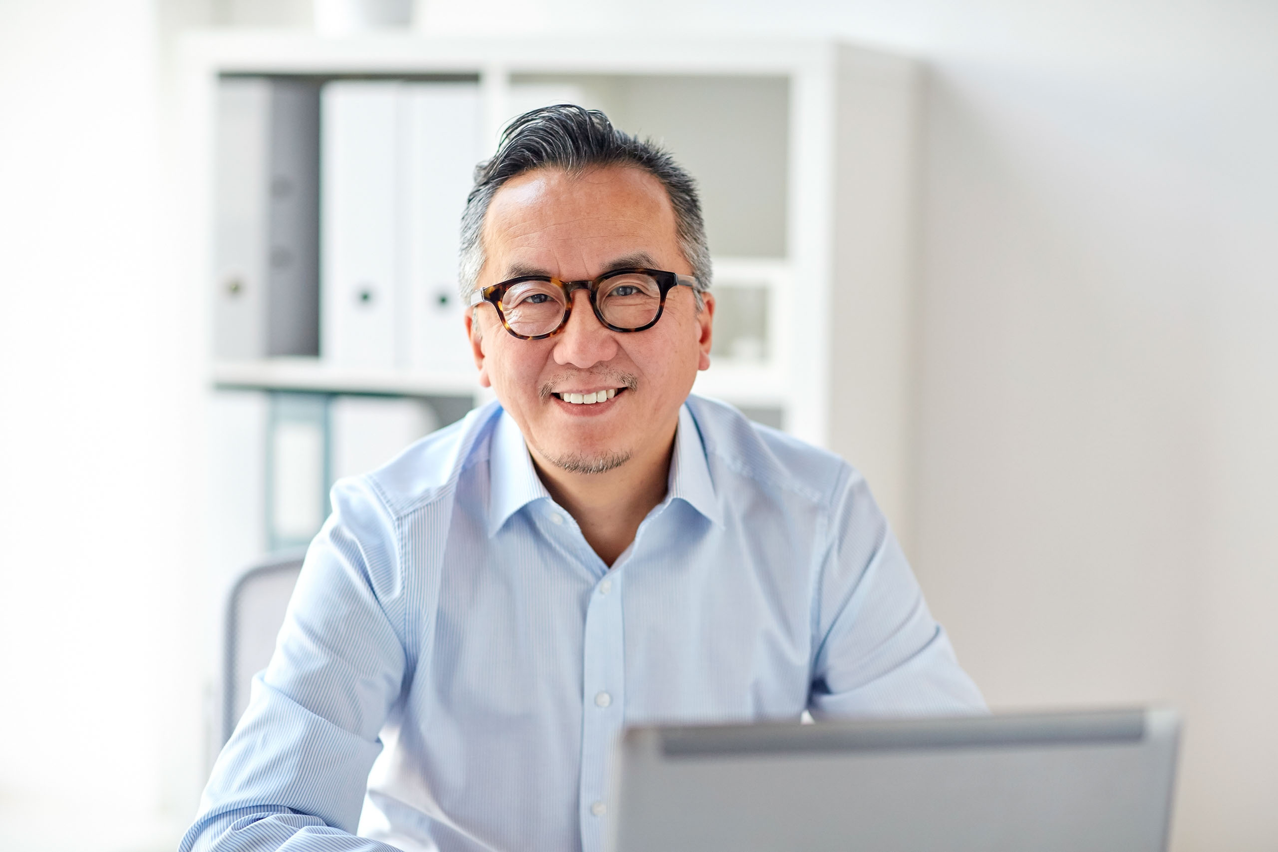 Glücklicher Geschäftsmann mit Brille und Laptop im Büro